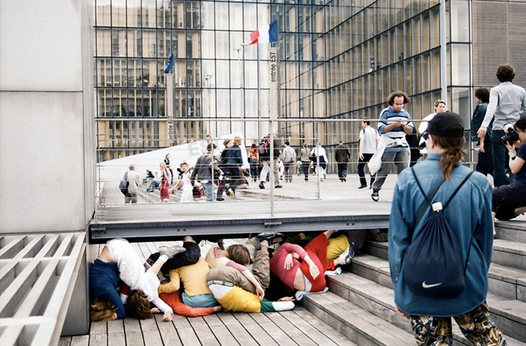 Menschen zusammengedrängt unter einer Plattform auf Treppen, Passanten schauen, Glasfassade im Hintergrund